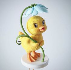 a yellow toy duck holding a flower on top of a white cake stand with blue flowers in it's beak