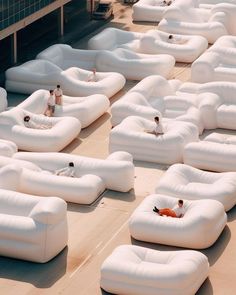 people are sitting on giant white couches in an open air area with one person laying on the floor