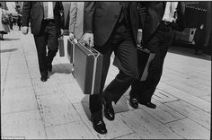 black and white photograph of three men in suits walking down the street with suitcases