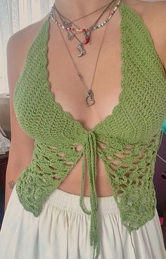 a woman wearing a green crochet halter top and white skirt with necklaces on her neck