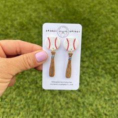 a pair of wooden earrings with white and red beads on them, in front of a green grass background