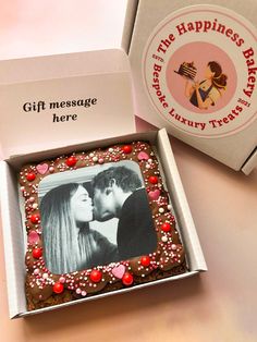 an open box with a chocolate cake in the shape of a kissing couple on it