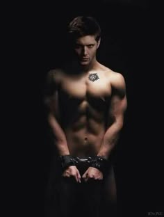 a shirtless man with his hands on his hips and handcuffs around his waist, standing in the dark