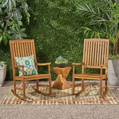 two wooden rocking chairs sitting next to each other in front of a green plant wall