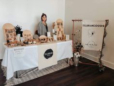 a woman standing in front of a table with wooden pieces on it and signs behind her