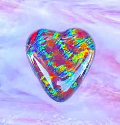 a heart shaped glass object sitting on top of a pink and blue background with white swirls