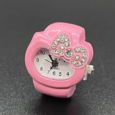 a close up of a small pink watch on a black surface with diamond eyes and hearts