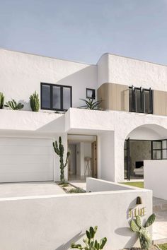 a white house with cactus plants in the front yard and an entry way leading to it