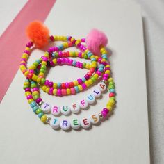 three bracelets with colorful beads and pom - poms are on a white surface