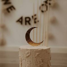 a white cake with a gold crescent decoration on top and the word are spelled in black