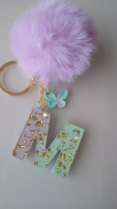 a keychain with the letter m on it and a fluffy ball hanging from it