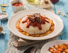 a plate with rice, meat and sauce on it next to other plates full of food