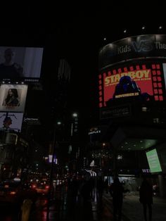 people are walking on the street at night in front of large billboards and buildings