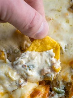 a hand dipping a tortilla chip into a casserole dish with cheese and vegetables