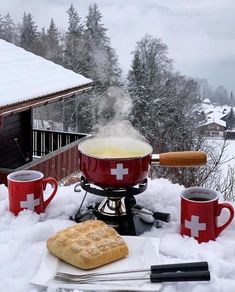 an outdoor cooking area covered in snow with two red mugs and one white cross on it