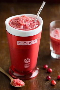 a glass filled with red liquid next to a spoon