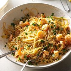 a white bowl filled with pasta and shrimp on top of a table next to silverware