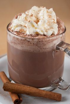 a cup of hot chocolate with whipped cream on top and cinnamon sticks next to it