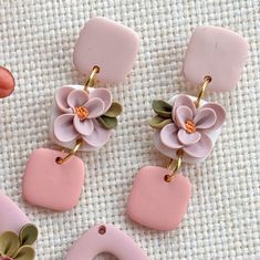 three pink and green flower shaped earrings on top of a white table cloth next to an orange object