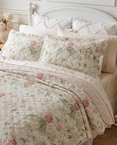 a white bed with pink flowers on it in a room next to a night stand