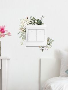 a white light switch sitting on top of a wall next to a vase with flowers