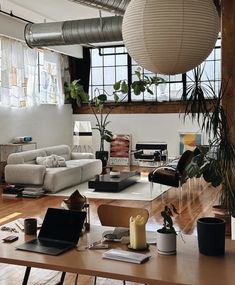 a living room filled with furniture and lots of windows next to a wooden floor covered in plants