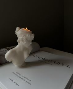 a white candle sitting on top of a book next to a lit candle in the shape of a lion