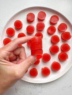 a white plate topped with sliced up pieces of red fruit next to a person's hand