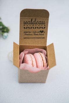 three pink macaroons in a cardboard box on a white table with green leaves