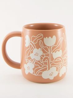 an orange coffee mug with white flowers painted on the outside and inside, sitting on a white surface