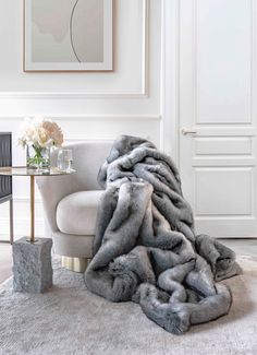 a living room with a couch and chair covered in a gray fur throw blanket next to a vase filled with flowers