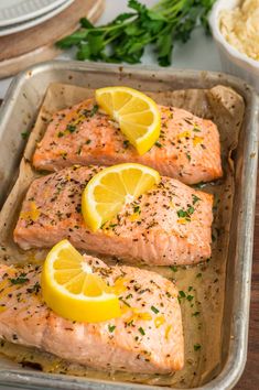 three salmon fillets in a baking pan with lemons and parsley on the side