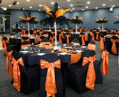 a banquet hall with tables covered in black and orange linens, decorated with palm trees