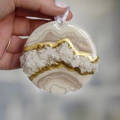 a hand holding a round ornament with white and gold decorations on it's side