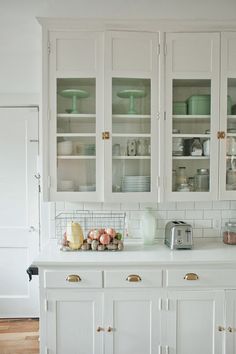 a white kitchen with lots of glass cabinets and dishes on top of it's counters