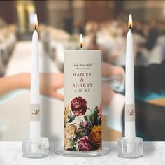 two white candles sitting next to each other on top of a marble table with flowers