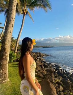 a beautiful woman standing on top of a lush green field next to the ocean with palm trees