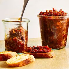 two jars filled with food sitting on top of a table next to bread and jam