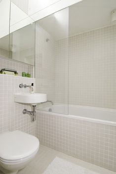 a white toilet sitting next to a bath tub in a bathroom under a large mirror