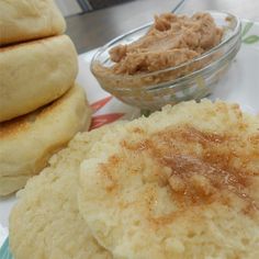 some food is sitting on a plate next to a bowl of peanut butter and two rolls