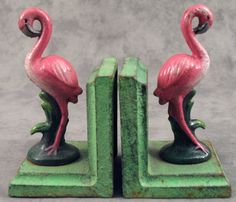 two pink flamingos are standing on green bookends, one is facing the other