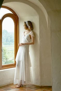 a woman standing in front of a window wearing a white dress and headband with her hands on her hips