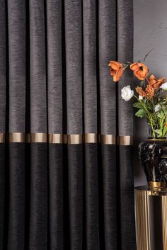 a vase filled with flowers sitting next to a window covered in black and gold curtains