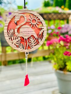 a pink flamingo wind chime hanging from a wooden deck with potted plants in the background