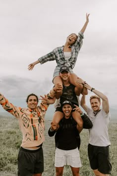 three men and one woman are standing in a field with their arms raised up to the sky