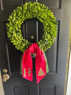 a wreath on the front door is decorated with green leaves and red ribbon as well as a monogrammed letter h