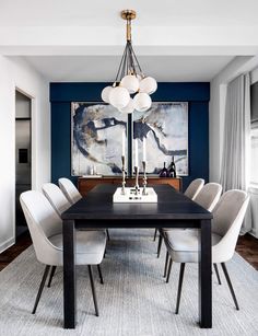 a dining room table with white chairs and a large painting on the wall behind it