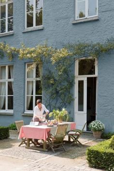 a man sitting at a table in front of a blue house with white trimmings