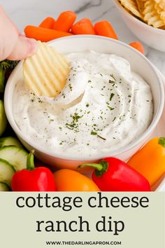 a hand dipping a cracker into a bowl of cottage cheese ranch dip surrounded by vegetables