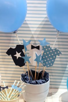 blue and white decorations in a bucket on a table with balloons, streamers and cake toppers